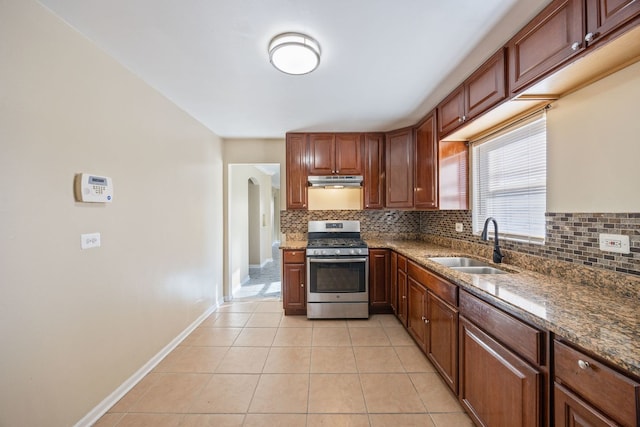 kitchen with light tile patterned flooring, sink, dark stone countertops, stainless steel range with gas stovetop, and backsplash