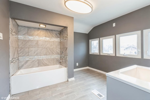 bathroom featuring tiled shower / bath, vanity, and vaulted ceiling