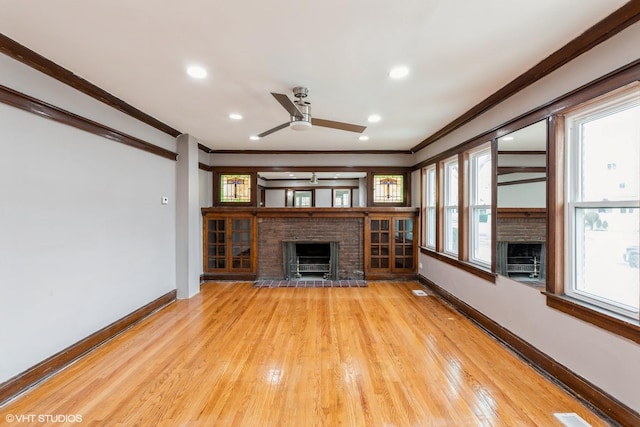 unfurnished living room with crown molding, plenty of natural light, a fireplace, and light hardwood / wood-style floors