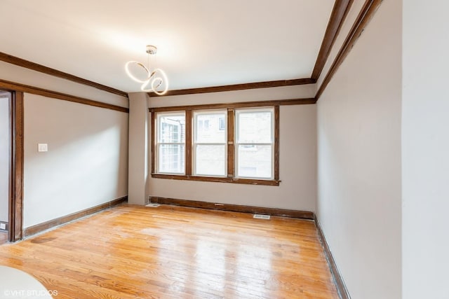 spare room with ornamental molding, an inviting chandelier, and light wood-type flooring