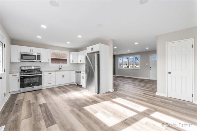 kitchen featuring sink, light stone counters, stainless steel appliances, light hardwood / wood-style floors, and white cabinets