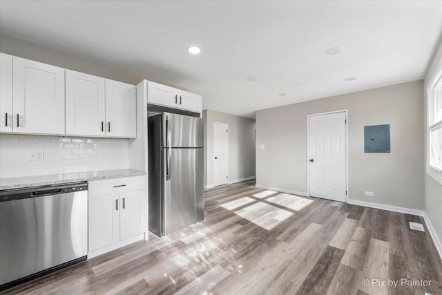 kitchen with appliances with stainless steel finishes, tasteful backsplash, light stone counters, wood-type flooring, and white cabinets