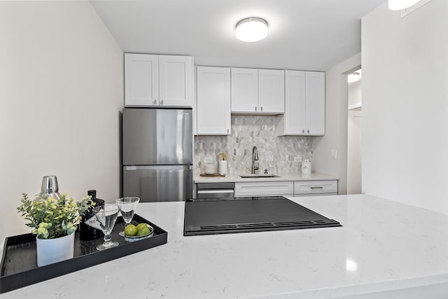 kitchen with sink, stainless steel refrigerator, white cabinetry, tasteful backsplash, and light stone countertops