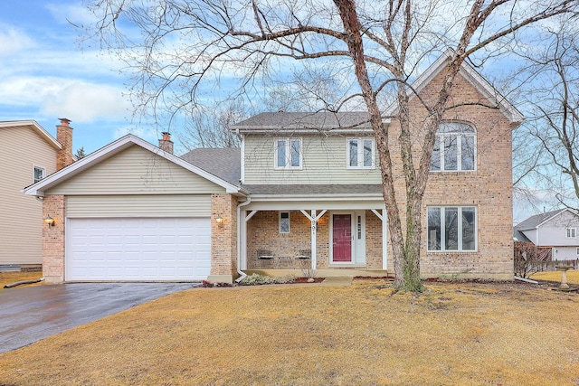 traditional-style house with aphalt driveway, a garage, brick siding, a chimney, and a front yard