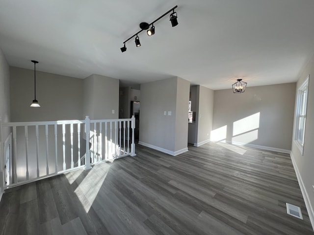 spare room featuring rail lighting, dark hardwood / wood-style floors, and an inviting chandelier