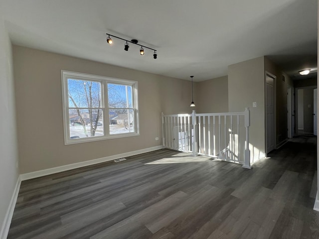 empty room featuring track lighting and dark hardwood / wood-style flooring