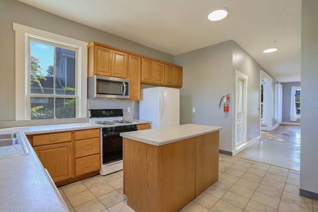 kitchen with a kitchen island, white refrigerator, light tile patterned floors, a healthy amount of sunlight, and gas range oven