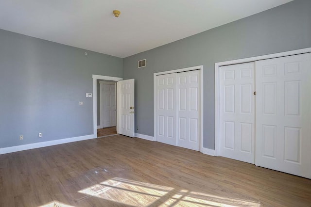 unfurnished bedroom featuring multiple closets and light hardwood / wood-style flooring