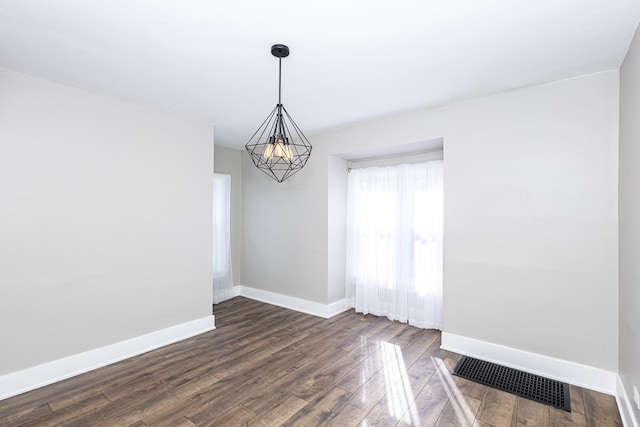 spare room featuring dark wood-type flooring and a chandelier