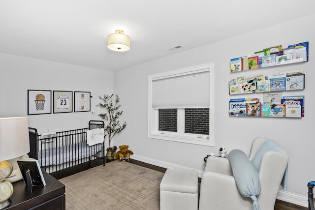 bedroom with a crib, baseboards, visible vents, and wood finished floors