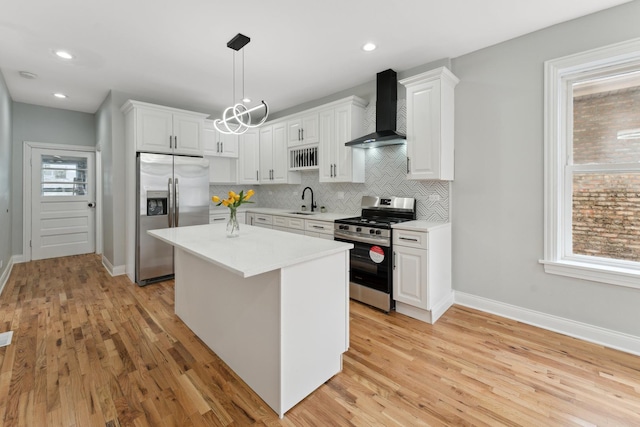 kitchen featuring appliances with stainless steel finishes, wall chimney range hood, white cabinets, and decorative light fixtures