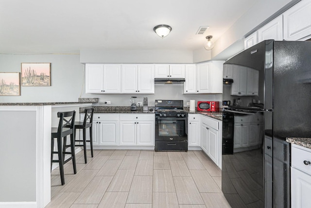 kitchen with dark stone countertops, black appliances, and white cabinets