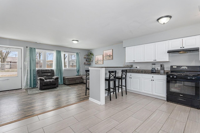 kitchen with a kitchen bar, kitchen peninsula, white cabinets, and black gas stove