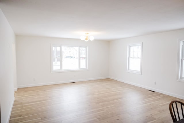 spare room with a notable chandelier, a wealth of natural light, and light hardwood / wood-style flooring