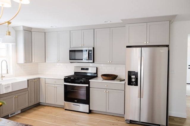 kitchen with appliances with stainless steel finishes, gray cabinets, light hardwood / wood-style floors, and sink