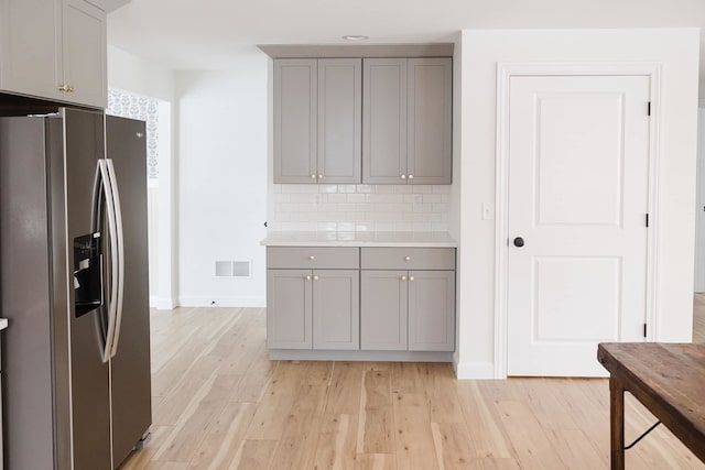 kitchen featuring tasteful backsplash, gray cabinets, stainless steel fridge with ice dispenser, and light hardwood / wood-style flooring