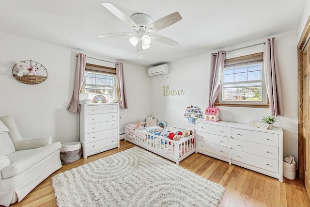 bedroom with light hardwood / wood-style flooring, a wall mounted air conditioner, a crib, and ceiling fan