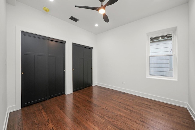 unfurnished bedroom featuring dark wood-type flooring, two closets, and ceiling fan