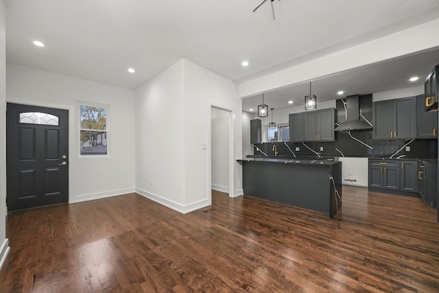 kitchen featuring gray cabinetry, decorative light fixtures, dark hardwood / wood-style floors, decorative backsplash, and wall chimney range hood