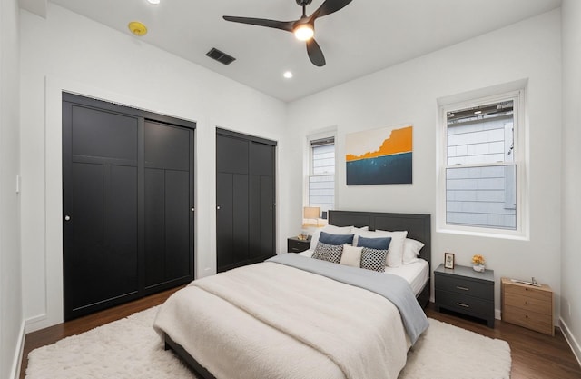 bedroom featuring dark wood-type flooring, two closets, and ceiling fan