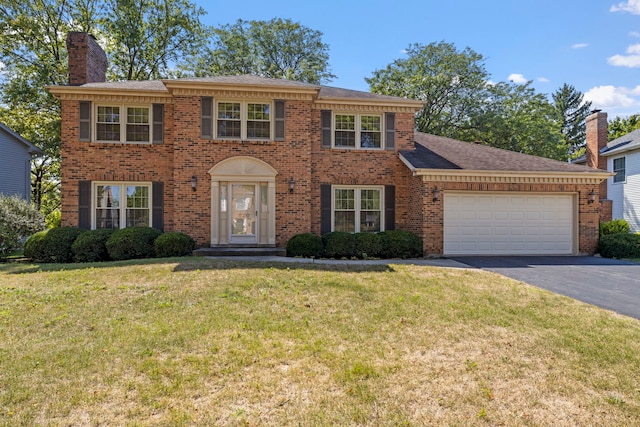 colonial inspired home featuring an attached garage, a front yard, driveway, brick siding, and a chimney