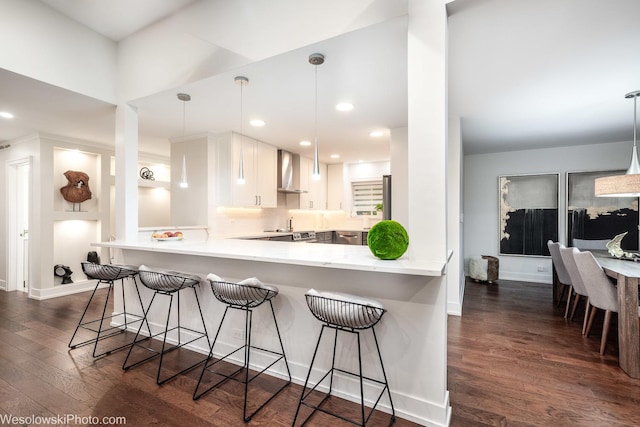 kitchen with hanging light fixtures, white cabinetry, wall chimney exhaust hood, and kitchen peninsula