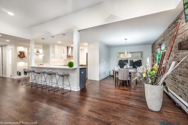 kitchen with hanging light fixtures, a kitchen breakfast bar, kitchen peninsula, brick wall, and white cabinets