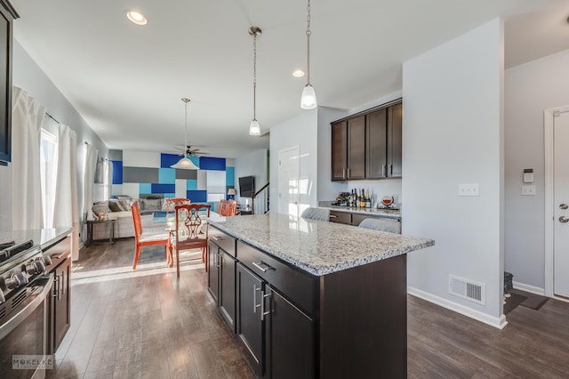 kitchen with light stone counters, a center island, stainless steel range oven, and dark brown cabinets