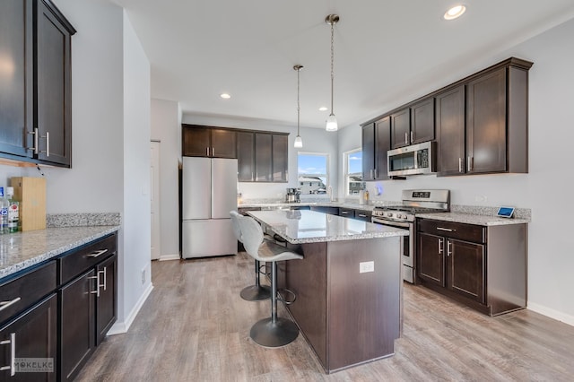 kitchen with appliances with stainless steel finishes, a kitchen breakfast bar, light stone countertops, decorative light fixtures, and light wood-type flooring