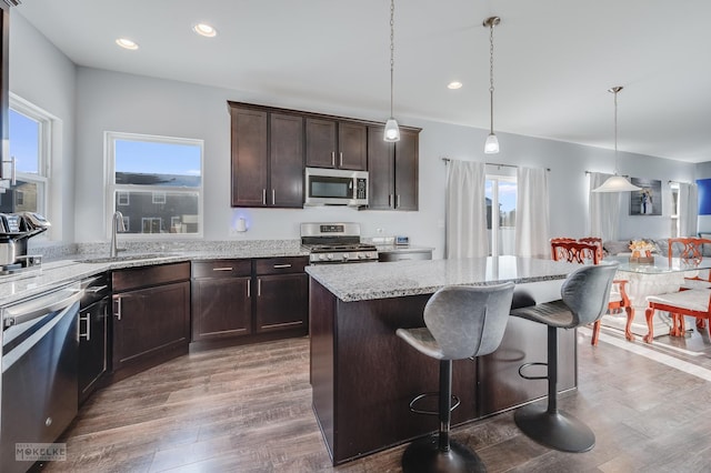 kitchen featuring a kitchen island, decorative light fixtures, sink, stainless steel appliances, and dark wood-type flooring