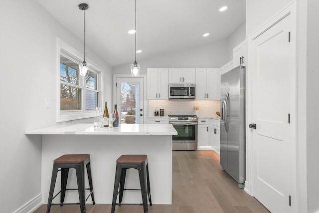 kitchen with a breakfast bar area, white cabinetry, appliances with stainless steel finishes, kitchen peninsula, and backsplash