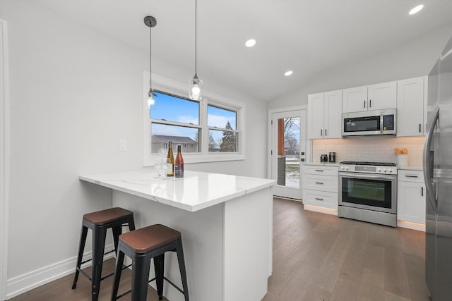 kitchen with pendant lighting, appliances with stainless steel finishes, white cabinets, a kitchen bar, and kitchen peninsula