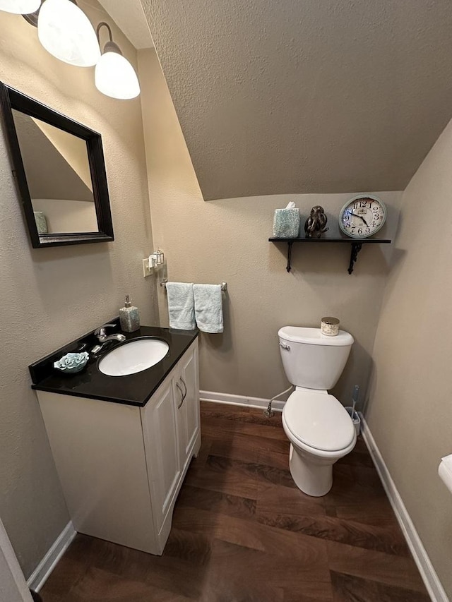 half bathroom featuring toilet, wood finished floors, vanity, baseboards, and vaulted ceiling