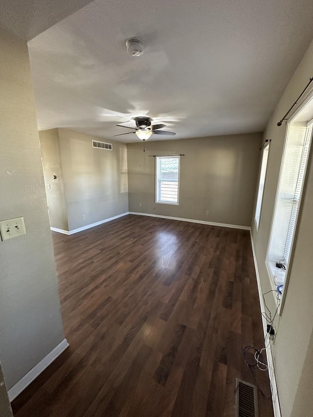 empty room featuring a ceiling fan, dark wood-style flooring, visible vents, and baseboards