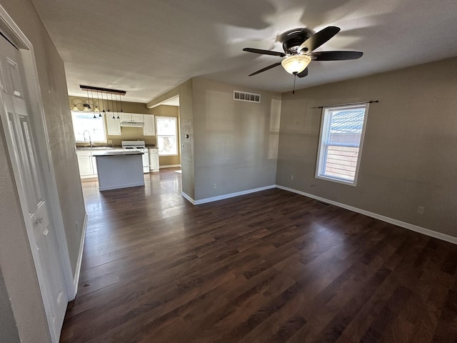 unfurnished living room featuring baseboards, visible vents, a ceiling fan, dark wood-type flooring, and a sink