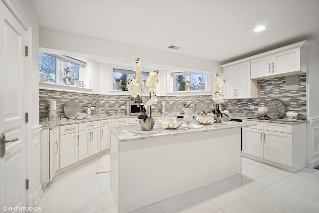 kitchen with a kitchen island, white cabinetry, decorative backsplash, light tile patterned floors, and light stone counters