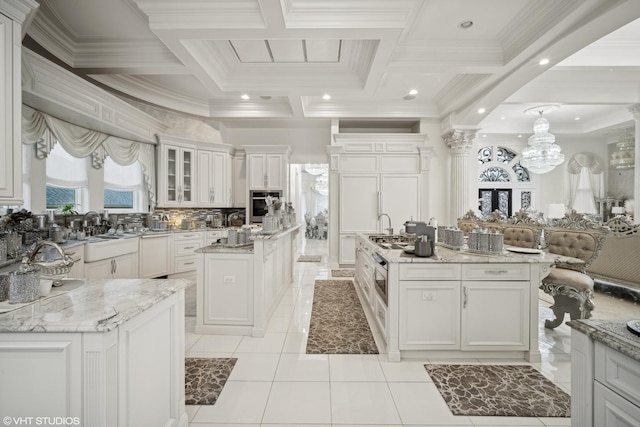 kitchen with white cabinetry, light stone countertops, oven, and an island with sink