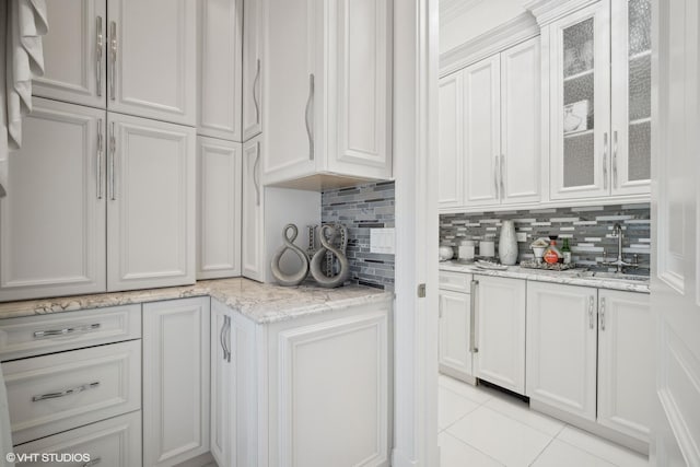 kitchen featuring sink, light tile patterned floors, backsplash, light stone counters, and white cabinets