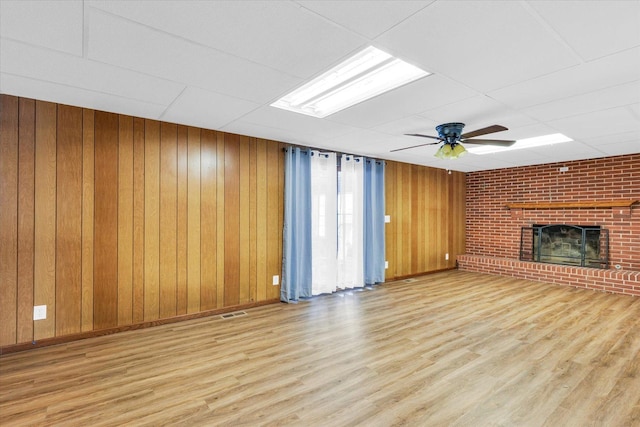 unfurnished living room featuring a drop ceiling, a fireplace, ceiling fan, and wood walls