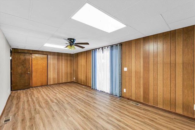 unfurnished room with a drop ceiling, ceiling fan, and wood walls