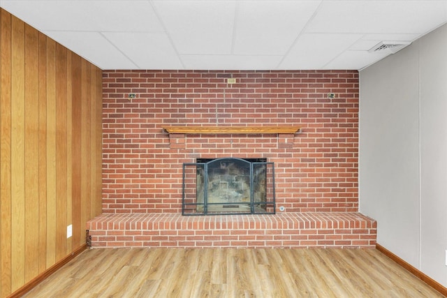 unfurnished living room with wood-type flooring, wooden walls, and a drop ceiling