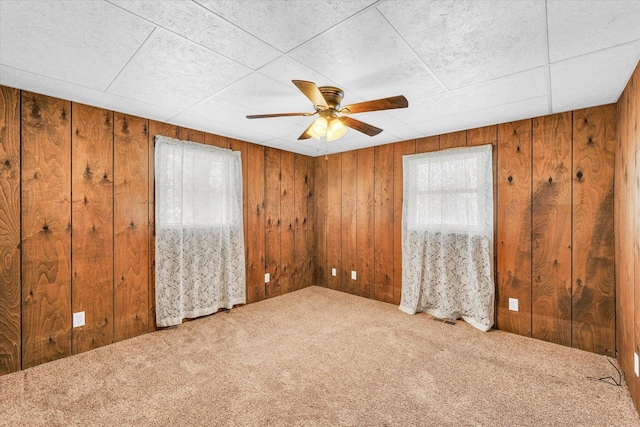 empty room with ceiling fan, wooden walls, and carpet floors