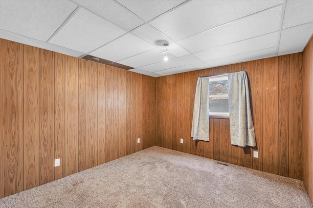 carpeted spare room featuring a paneled ceiling and wooden walls