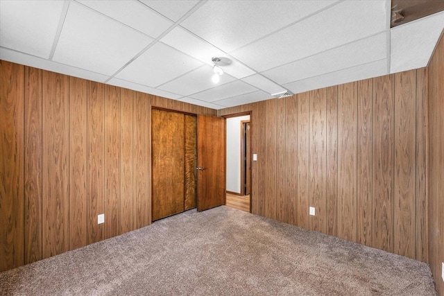 unfurnished room with a drop ceiling, carpet floors, and wooden walls