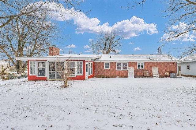 snow covered back of property featuring a sunroom and central air condition unit