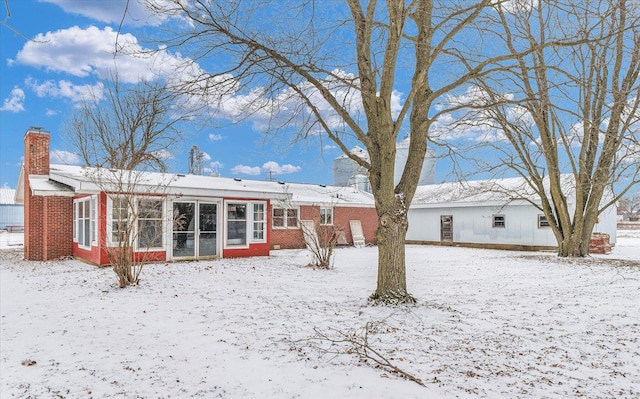 snow covered rear of property with a sunroom