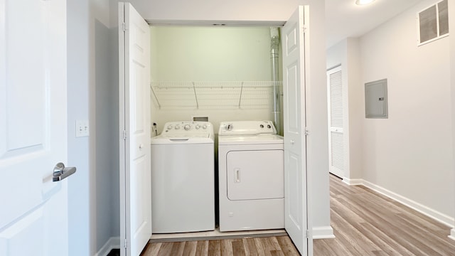 clothes washing area with separate washer and dryer, electric panel, and light wood-type flooring