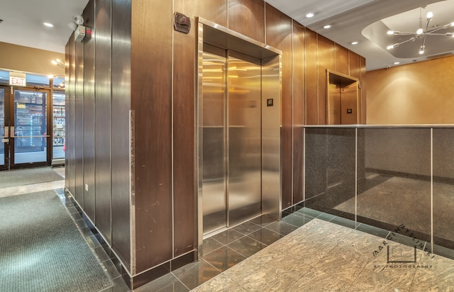 interior space featuring a notable chandelier, wooden walls, and elevator