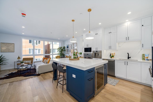 kitchen with a kitchen island, appliances with stainless steel finishes, decorative light fixtures, white cabinetry, and light wood-type flooring