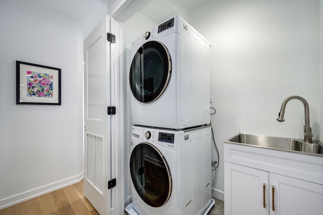 laundry room with stacked washing maching and dryer, sink, and light hardwood / wood-style floors